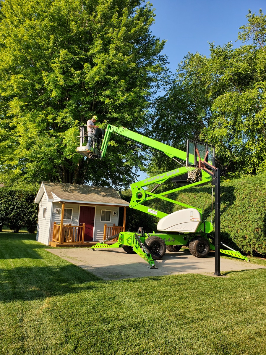 green tree crane in a backyard with a man in it going up